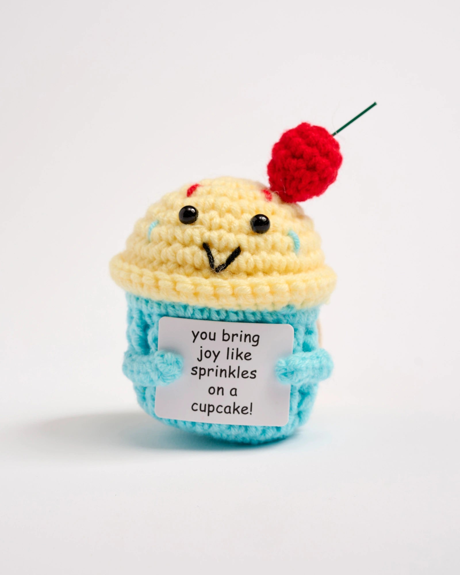 Crocheted cupcake toy with a cherry on top and a message tag on a white background
