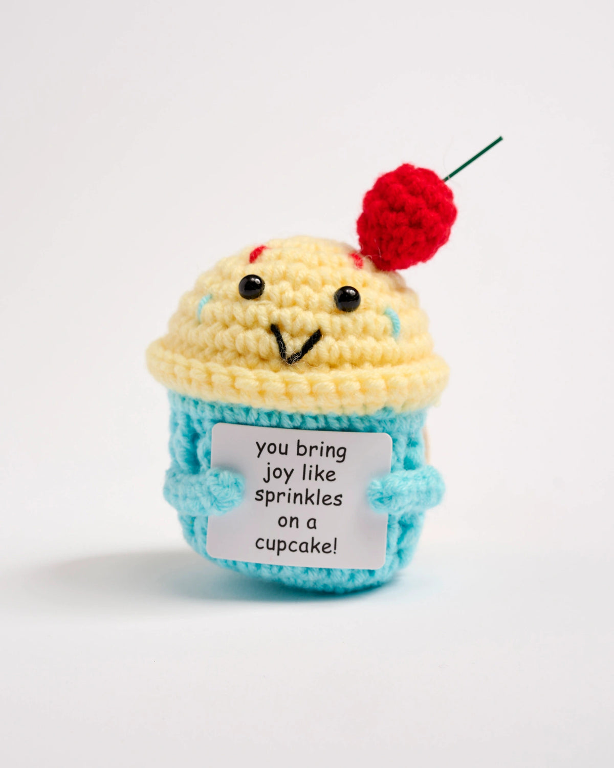Crocheted cupcake toy with a cherry on top and a message tag on a white background